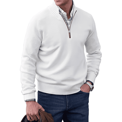 Mann in weißem Pullover mit Reißverschluss, blaue Jeans, Uhr, hält braune Jacke.