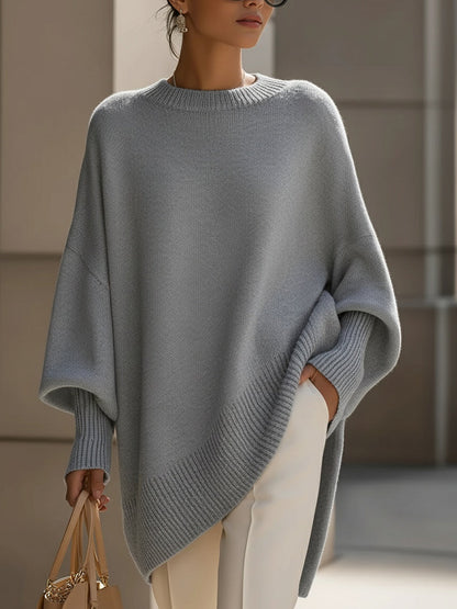 Modell i grå stickad poncho med ribbade muddar, vita byxor och handväska 10