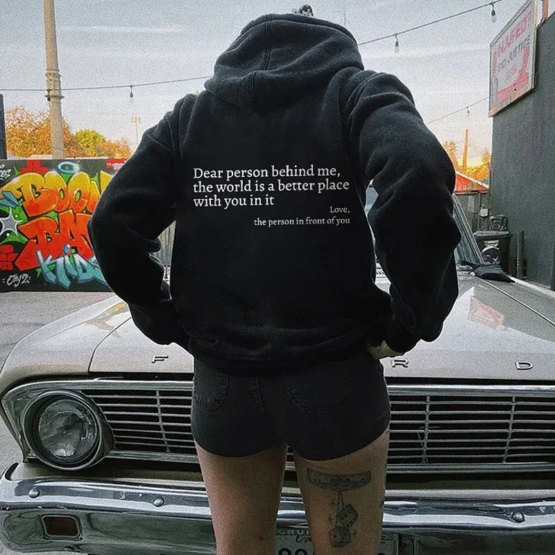 Person in schwarzem Hoodie mit Aufschrift vor klassischem Ford-Auto, urbaner Hintergrund.