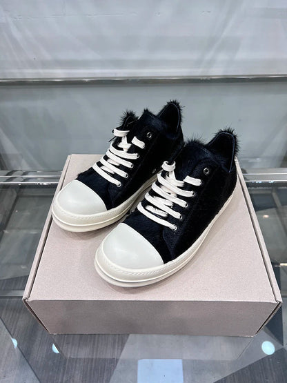 Schwarze Fell-Sneaker mit weißen Schnürsenkeln und Sohlen auf Karton, modische Freizeitschuhe.