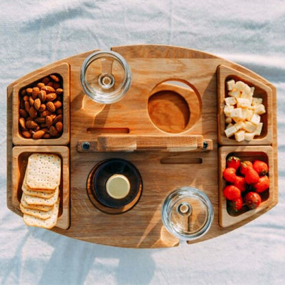 Holz-Picknicktisch mit Snacks, Wein und Gläsern, ideal für Outdoor-Aktivitäten und Gartenpartys.
