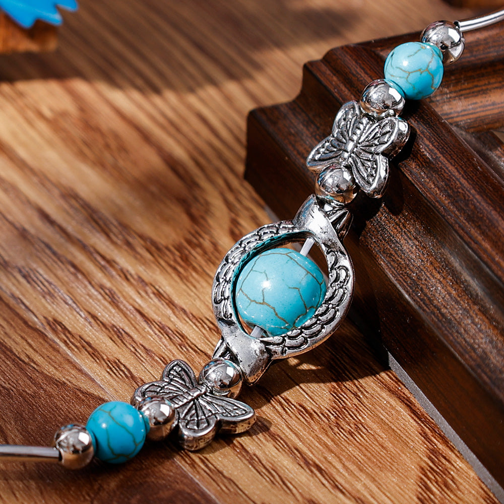 Silbernes Armband mit türkisfarbenen Steinen und Schmetterlingsdesign auf Holzoberfläche.