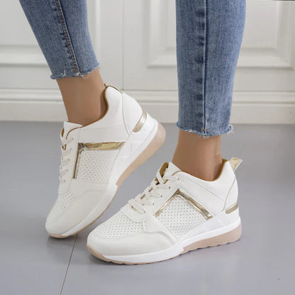 Weiße Damen-Sneaker mit goldenen Akzenten, perforiertem Design, getragen mit blauen Jeans.