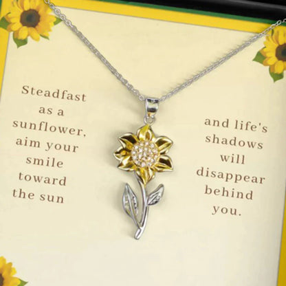 Silberne Sonnenblumen-Halskette mit gelbem Blütenanhänger auf Geschenkbox mit Zitat.