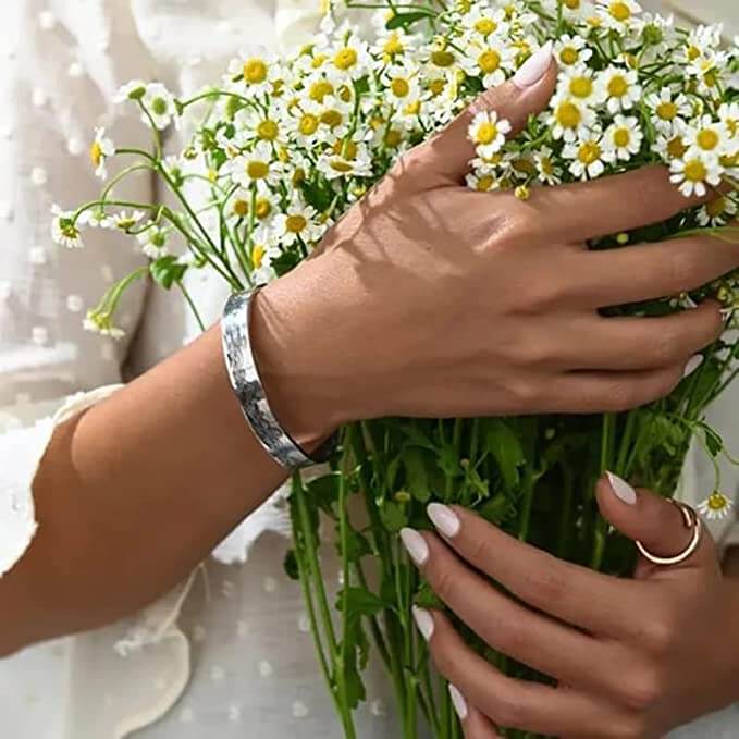 Frau hält Gänseblümchenstrauß, trägt silbernes Armband und Ring, weiße Bluse.
