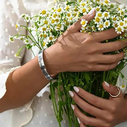 Frau hält Gänseblümchenstrauß, trägt silbernes Armband und Ring, weiße Bluse.