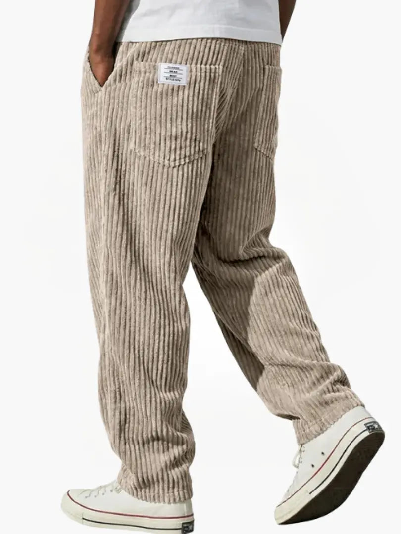Beige manchesterbyxa bakifrån på gående modell, med breda ränder, bakficka, liten etikett och vita sneakers. 3