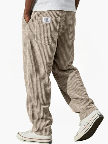 Beige manchesterbyxa bakifrån på gående modell, med breda ränder, bakficka, liten etikett och vita sneakers. 3