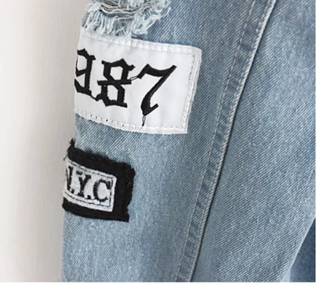 Zerrissene blaue Jeans mit Aufnähern "1987" und "N.Y.C.", modisch, lässig, Denim-Stoff.