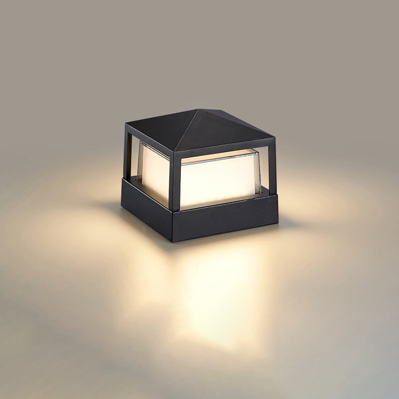 Fyrkantig svart lampa med pyramidformat tak och lysande vit skärm på neutral bakgrund. 10