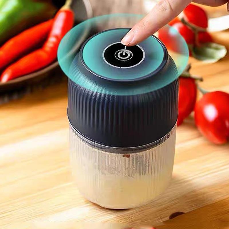 Närbild på ett finger som trycker på strömknappen ovanpå den mörkblå matberedaren, med röd chili och tomater i bakgrunden. 2