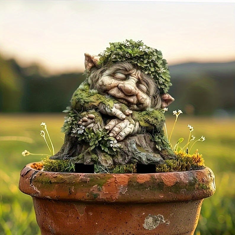 Närbild på sovande troll med bladkrans och mossiga armar, placerat i en terrakottakruka med gula smårblommor. 17