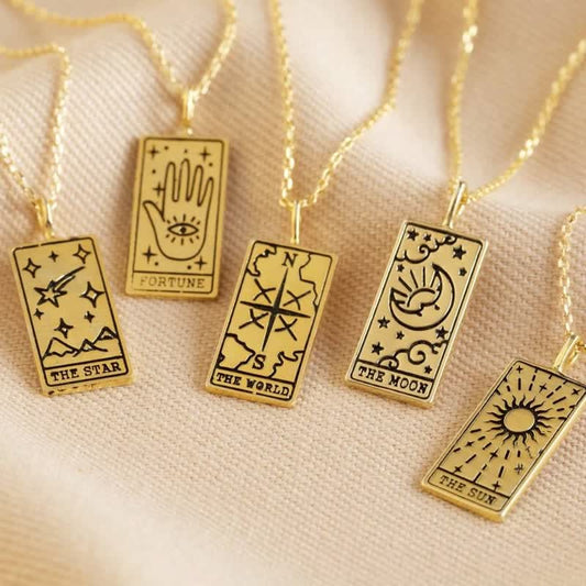 Goldene Tarot-Anhänger mit Ketten, Symbole: Stern, Hand, Welt, Mond, Sonne, auf beigem Stoff.