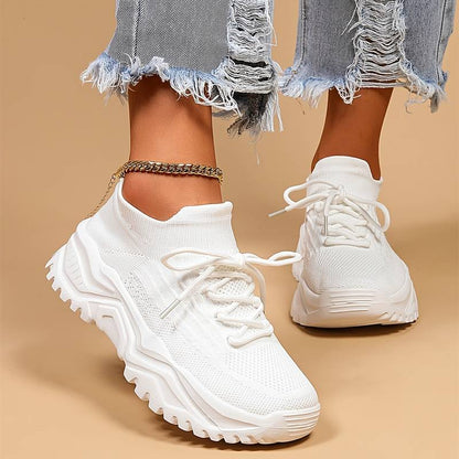 Weiße Damen-Sneaker mit dicker Sohle, gestricktem Obermaterial und zerrissenen Jeans.