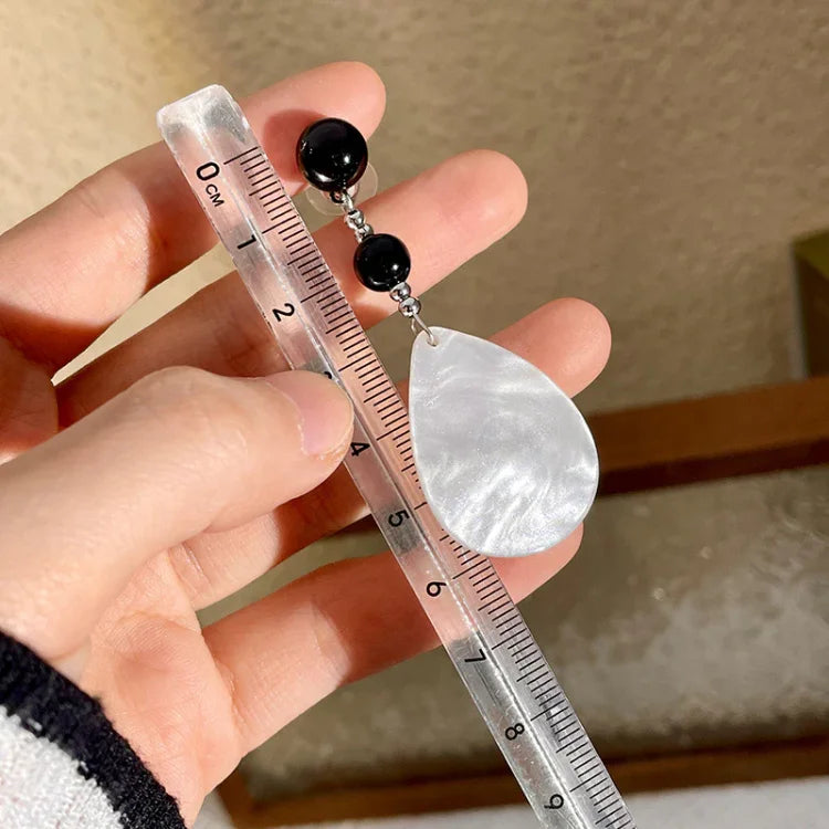 Hand hält Lineal mit silbernem Tropfen-Ohrring und schwarzen Perlen, Schmuckdesign, Nahaufnahme.
