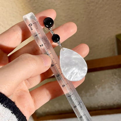 Hand hält Lineal mit silbernem Tropfen-Ohrring und schwarzen Perlen, Schmuckdesign, Nahaufnahme.