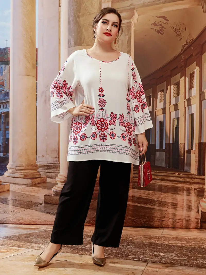 Frau in weißer Tunika mit roten Blumenmustern, schwarze Hose, goldene Schuhe, elegante Mode.