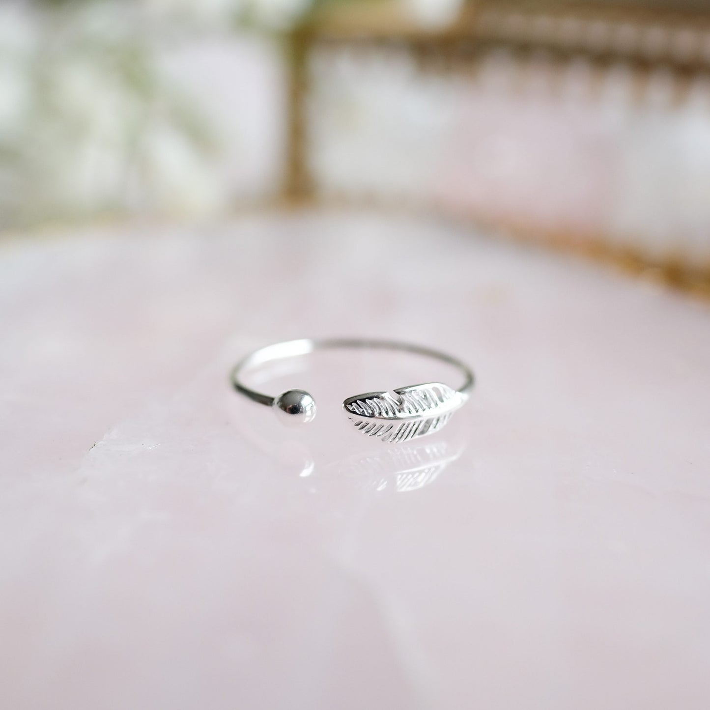 Silberner offener Ring mit Federdesign auf rosa Hintergrund, minimalistischer Schmuck.