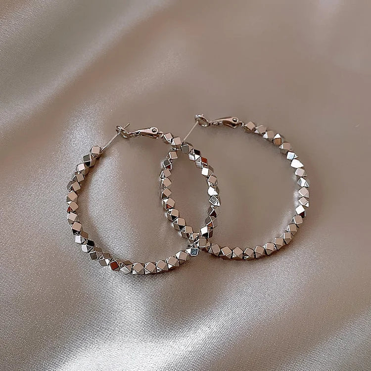 Silberne Creolen Ohrringe, facettierte Oberfläche, eleganter Schmuck auf Satin-Hintergrund.