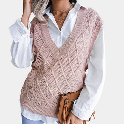 Frau in rosa Strickweste über weißer Bluse, hält braune Lederhandtasche, modisch, elegant.