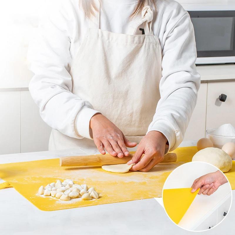 Person rollt Teig auf gelber Silikon-Backmatte in Küche, mit Nudelholz und Mehl.