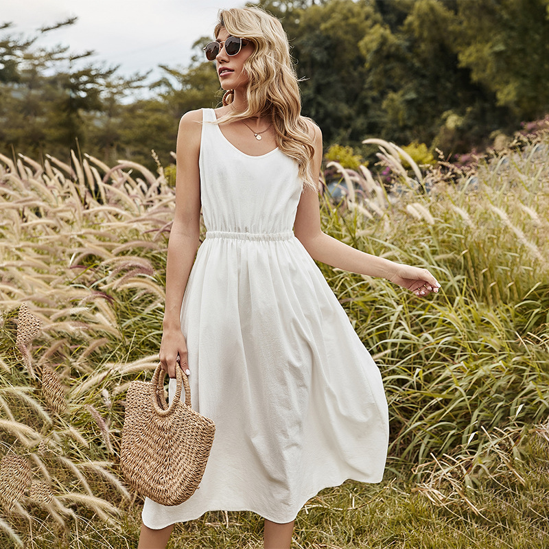 Frau im weißen Sommerkleid mit Strohtasche in einem Feld, Sonnenbrille, blonde Haare.