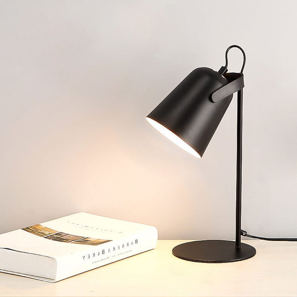 Svart bordslampa med skärmen vänd åt vänster, tänd på en ljus träskiva bredvid en uppslagen bok. 12