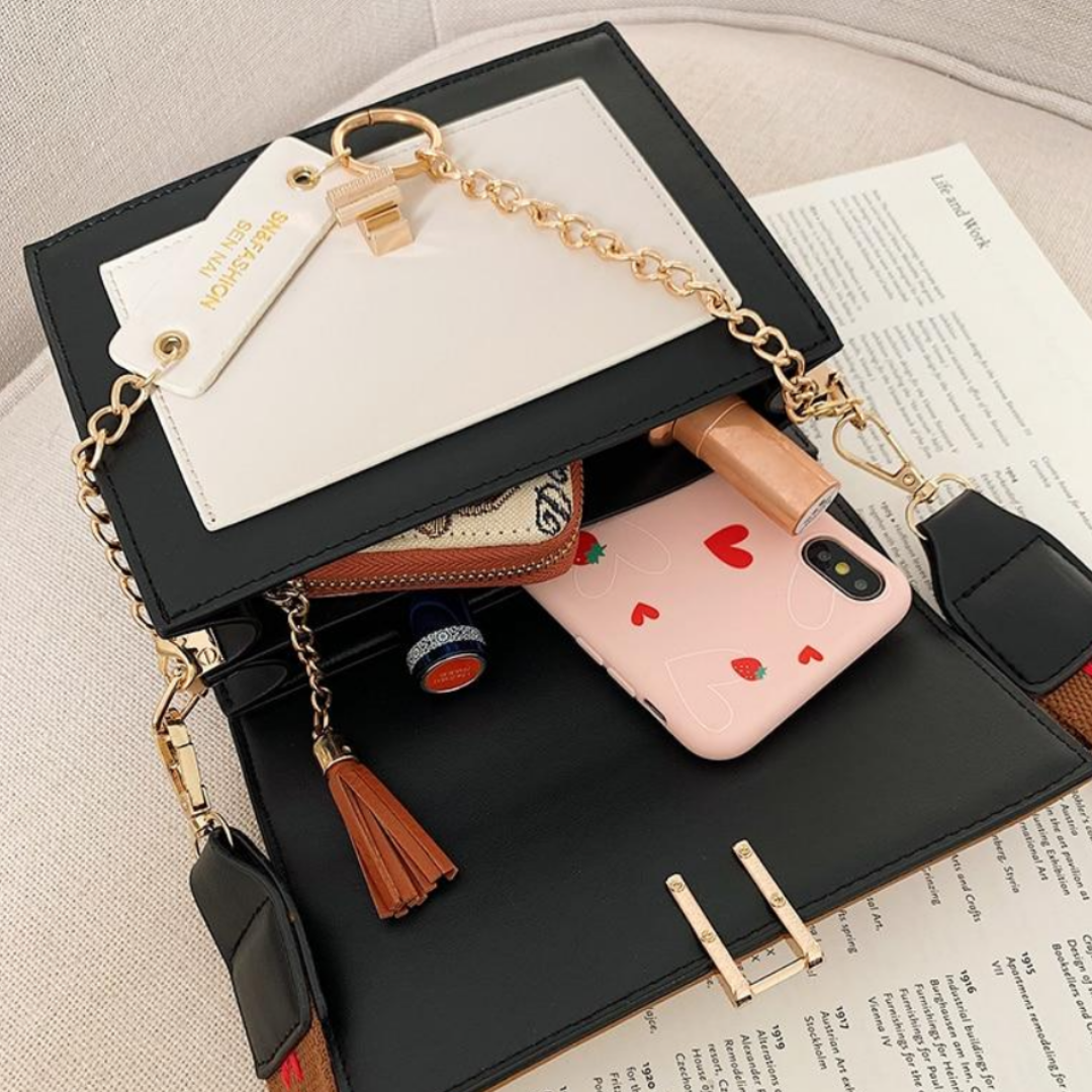 Schwarze Handtasche mit goldener Kette, Leder, enthält Smartphone und Kosmetikartikel.