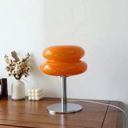 Orangefarbene Tischlampe aus Glas auf Holztisch, moderne Inneneinrichtung, minimalistisches Design.