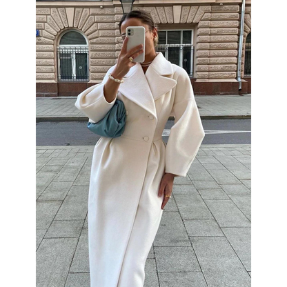 Frau in weißem Wollmantel mit blauer Tasche, fotografiert auf städtischer Straße.