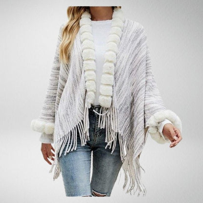 Frau in grauem Strickponcho mit Fransen und weißem Kunstfell, lässige Mode.