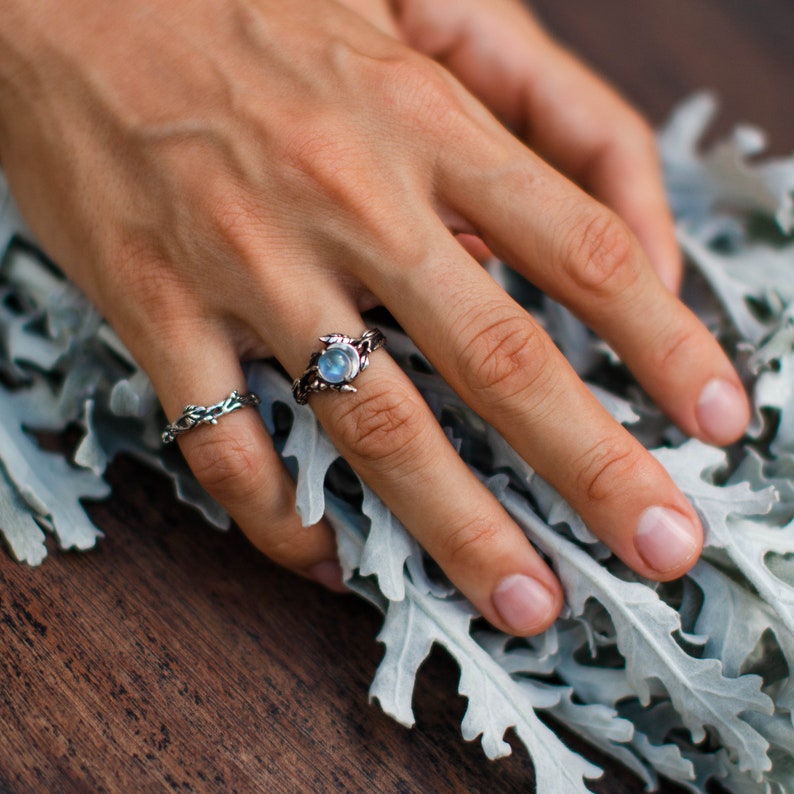 Hand mit silbernem Ring und blauem Stein auf grauen Blättern, Schmuck, Modeaccessoire.