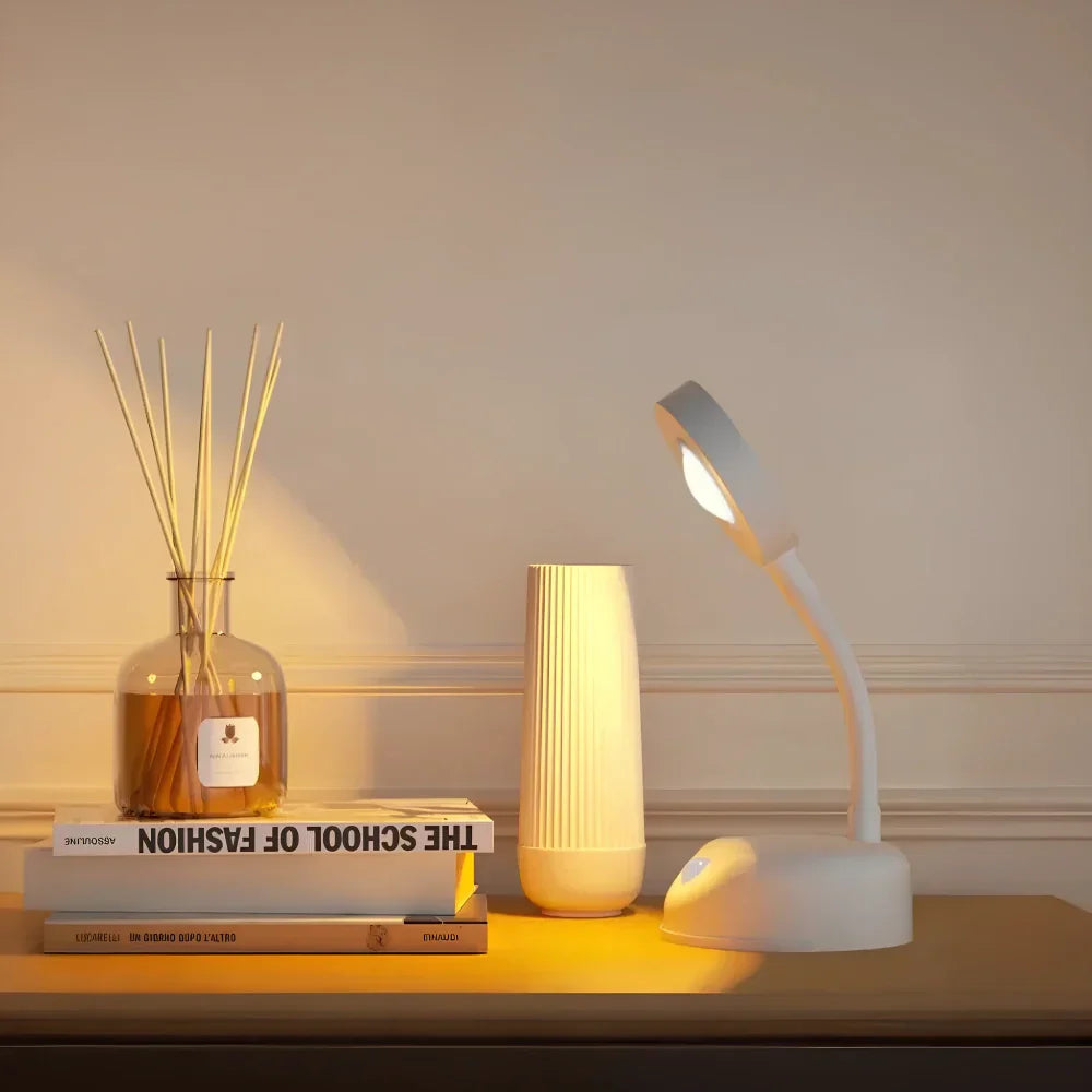 Moderne LED-Schreibtischlampe in Weiß auf Holzoberfläche, neben Duftstäbchen und Vase.
