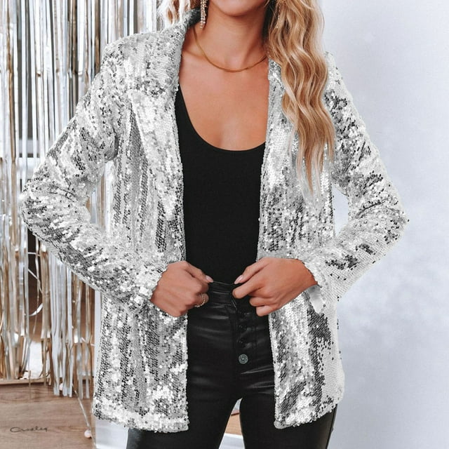 Frau in silbernem Paillettenblazer, schwarzem Top und Lederhose vor silbernem Hintergrund.