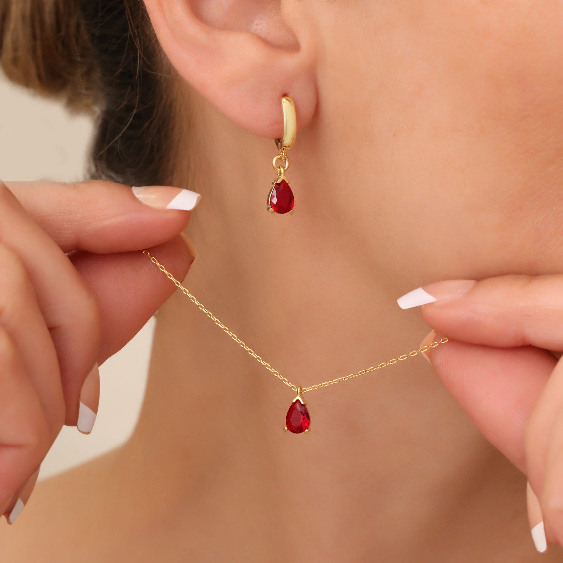 Frau trägt goldene Ohrringe und Halskette mit roten Tropfenanhängern, eleganter Schmuck.