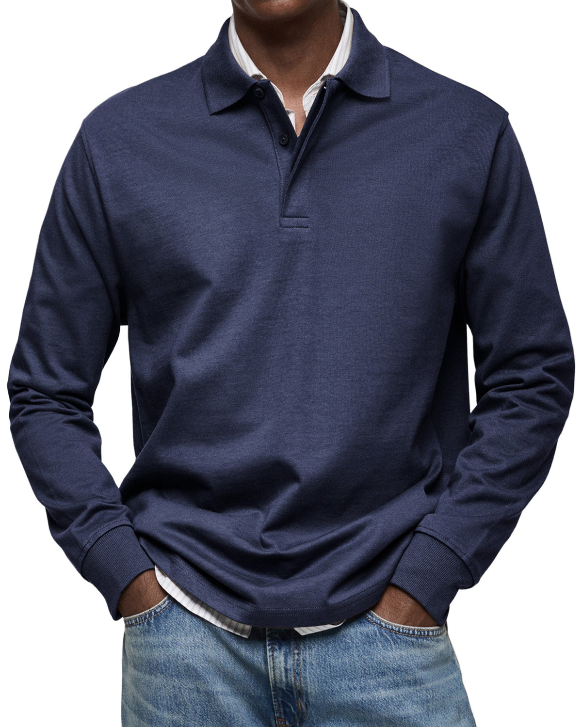 Marinblå långärmad pikétröja sedd framifrån på en modell med händerna i fickorna, över randig skjorta och jeans. 3