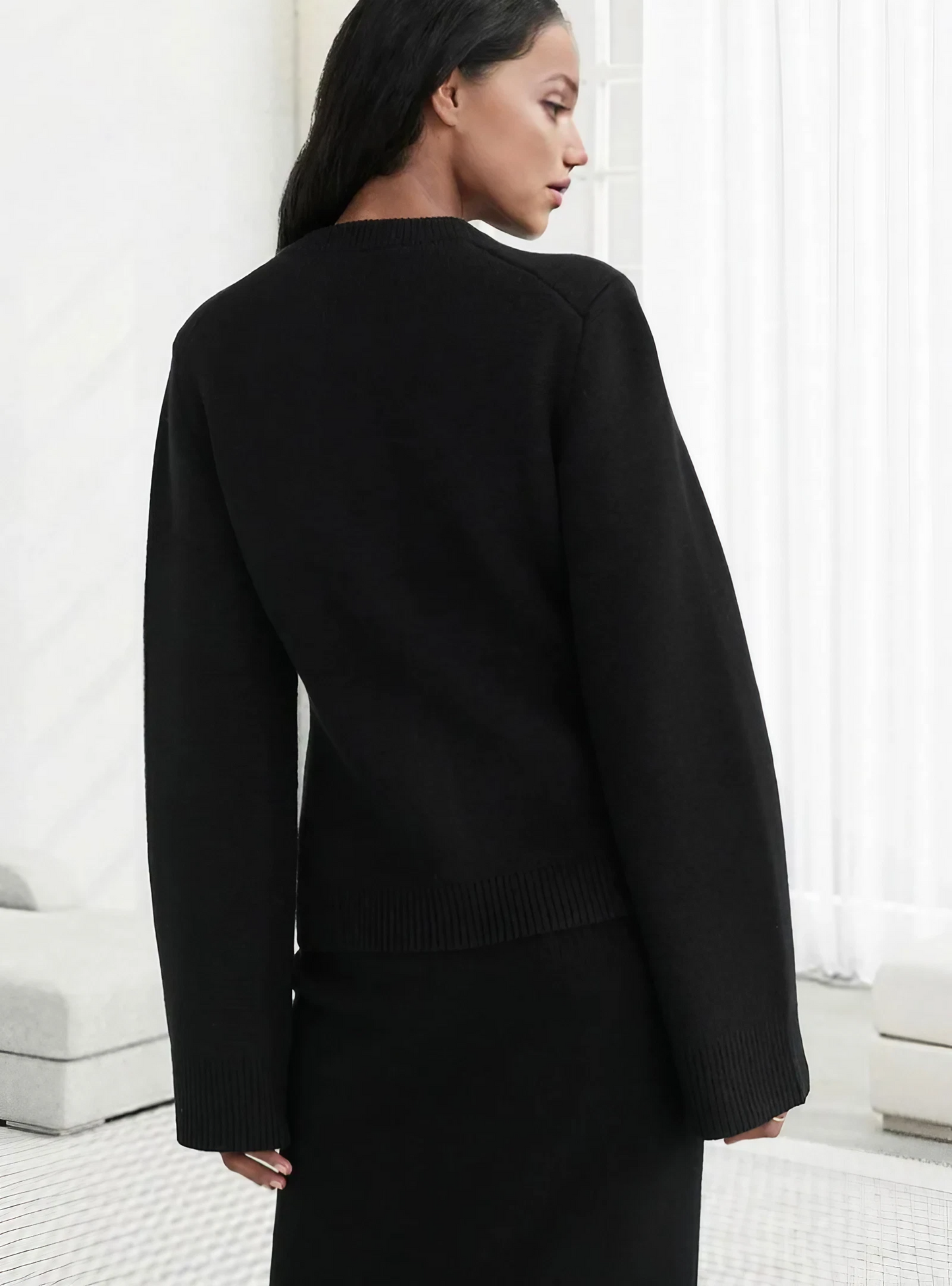 Frau in schwarzem Pullover und Rock, elegantes Outfit, moderne Mode, minimalistisch, seitlich.