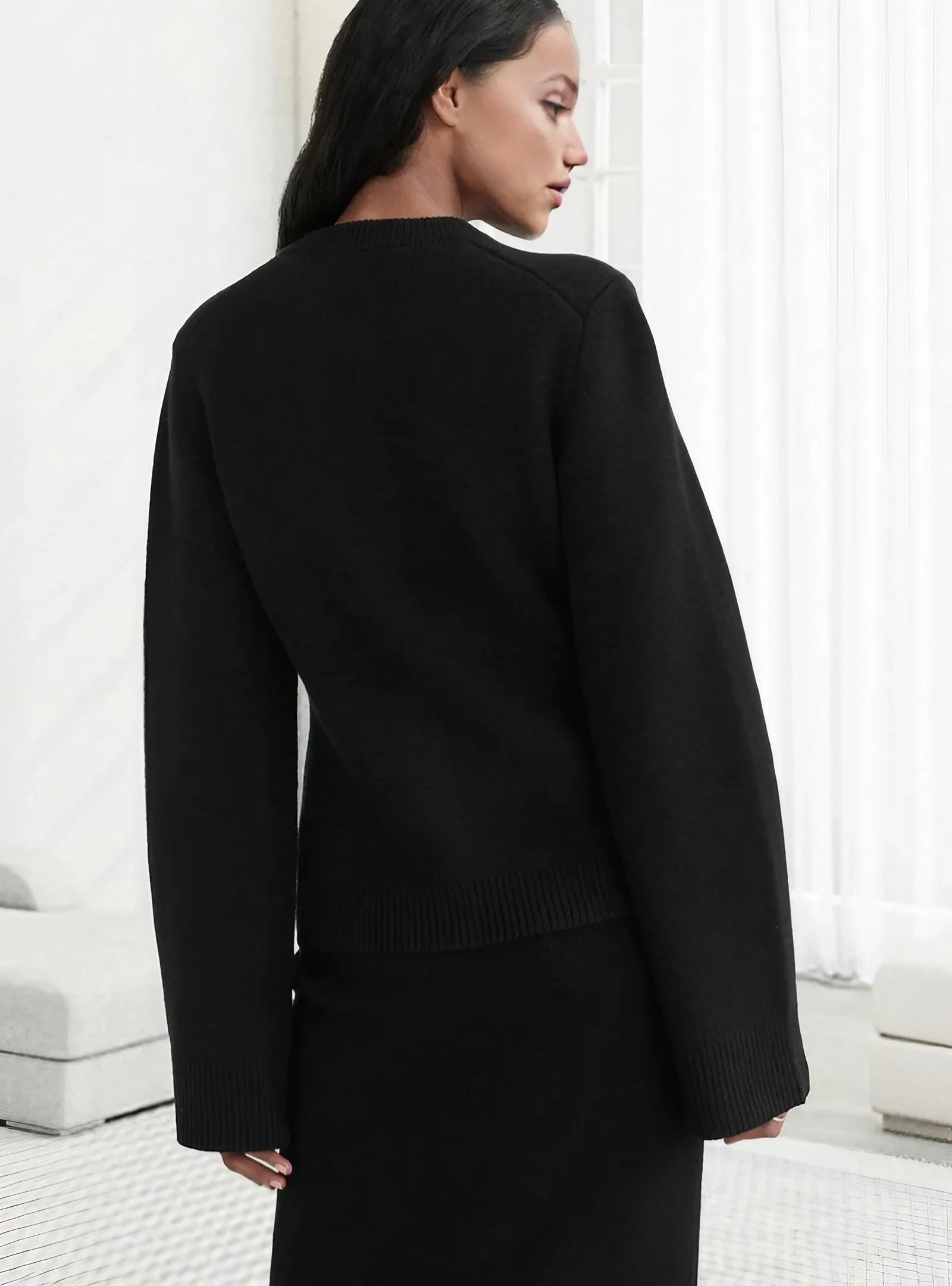 Frau in schwarzem Pullover und Rock, elegantes Outfit, moderne Mode, minimalistisch, seitlich.