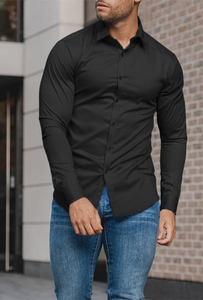 Mann in schwarzem Hemd und blauer Jeans vor Backsteinwand, modische Herrenbekleidung.