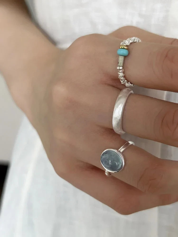 Hand mit drei Silberringen, einer mit blauem Stein, auf weißem Hintergrund.