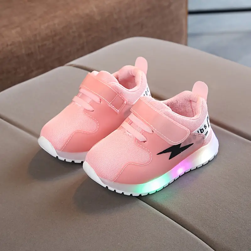 Rosa LED-Kinderschuhe mit Klettverschluss, Blitz-Design, auf grauem Sofa.
