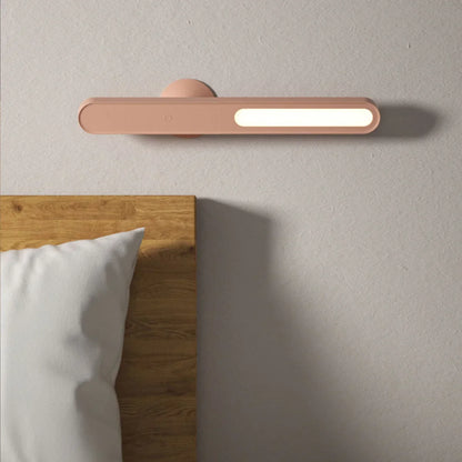 Moderne LED-Wandleuchte in Rosa über Holz-Bettkopfteil, minimalistisch, energiesparend.