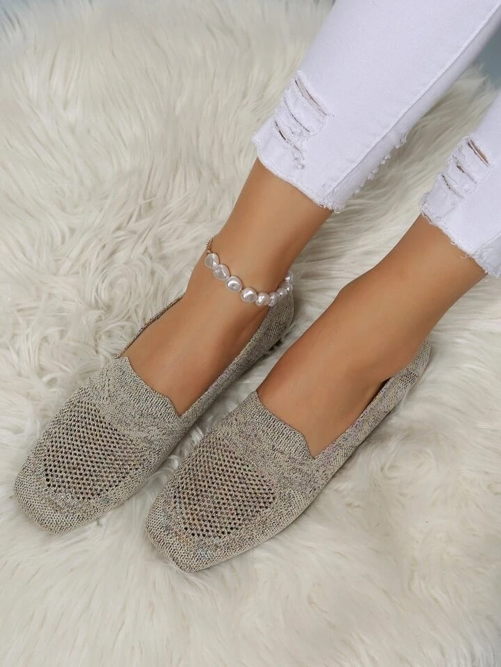 Grå-beige mesh-skor med fyrkantig tå sedda uppifrån på en modell i trasiga vita jeans och pärlankelkedja, på vit lurvig matta. 20