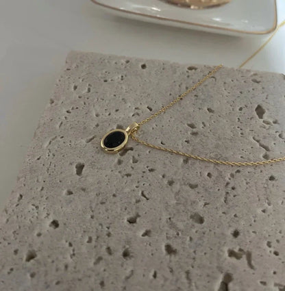 Goldene Halskette mit schwarzem Anhänger auf Steinplatte, eleganter Schmuck, minimalistisch.