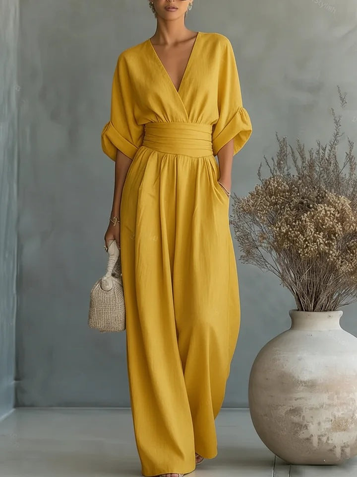Jumpsuiten i senapsgult, buren av en kvinna med flätad handväska bredvid en stor kruka med torkade blommor. 3