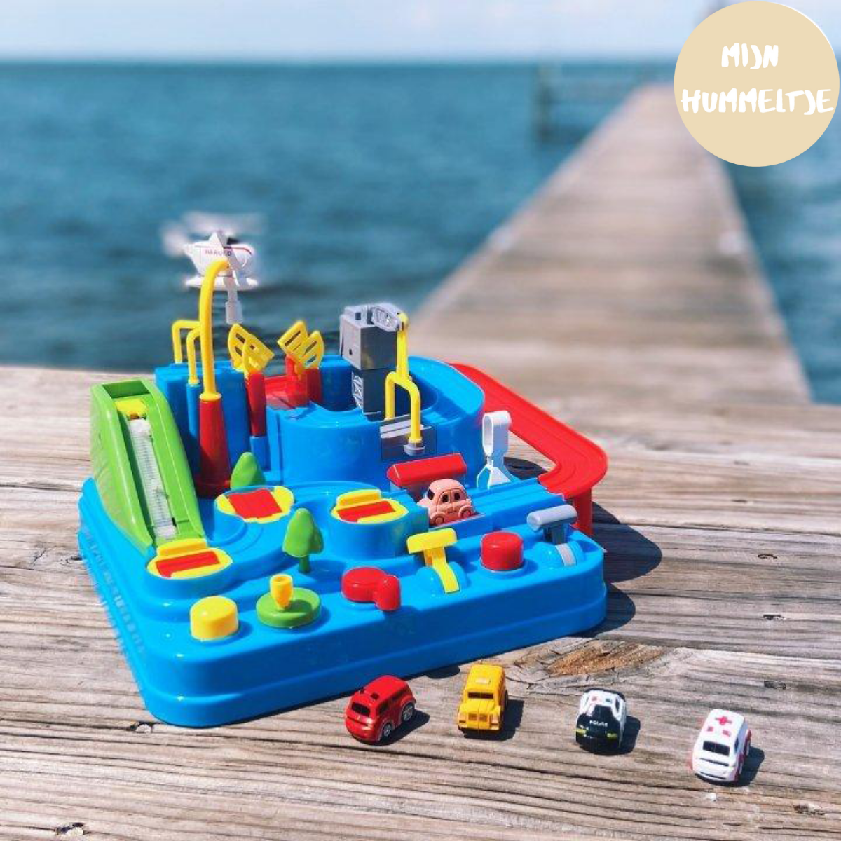 Buntes Spielzeug-Set mit Autos und Stadtlandschaft auf Holzsteg am Meer.