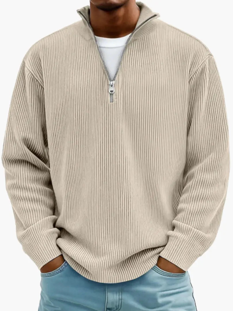Man i beige ribbstickad tröja med dragkedjekrage, vit t-shirt under och händerna i fickorna på ljusblå jeans. 4