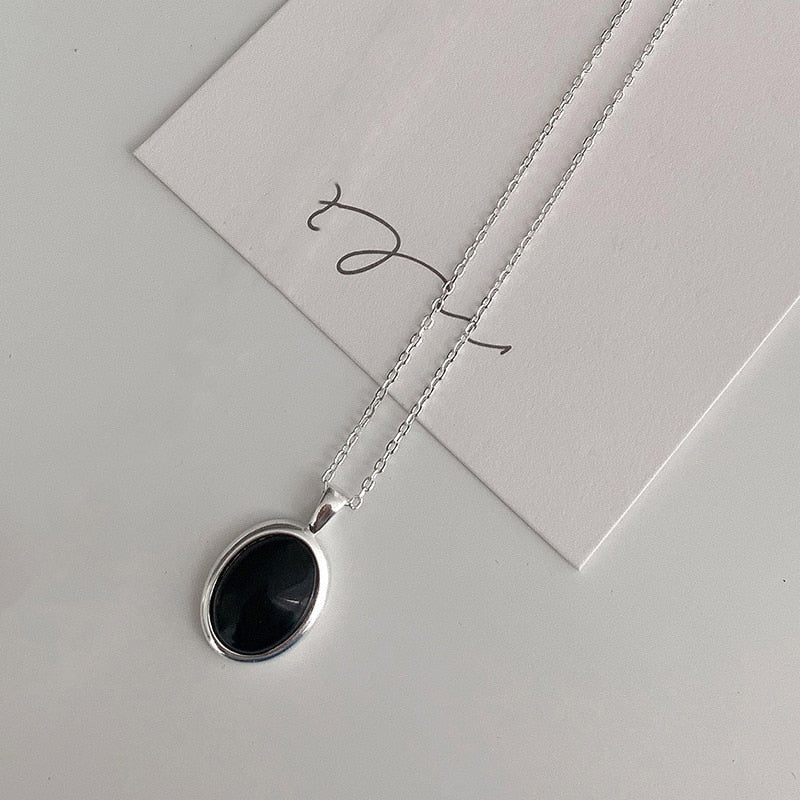 Silberkette mit ovalem schwarzem Anhänger auf weißem Hintergrund, eleganter Schmuck.