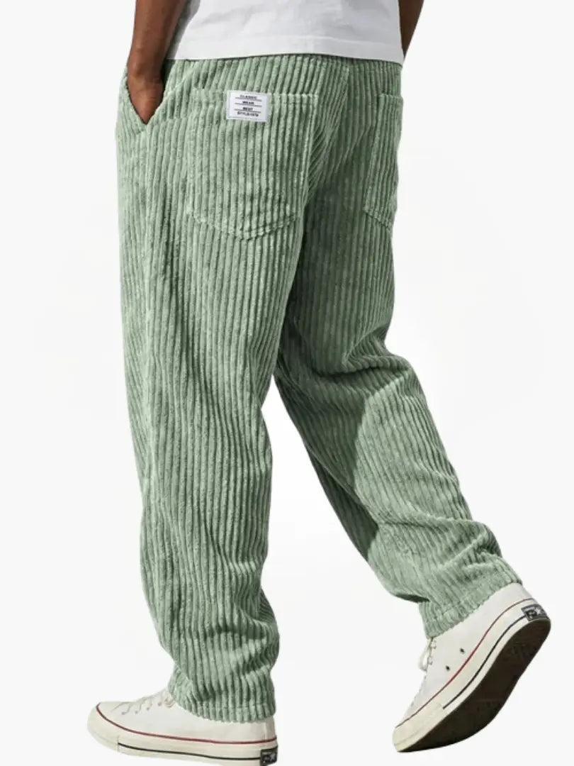 Ljusgrön manchesterbyxa bakifrån på gående modell med vit t-shirt, bakficka, liten etikett och vita sneakers. 4