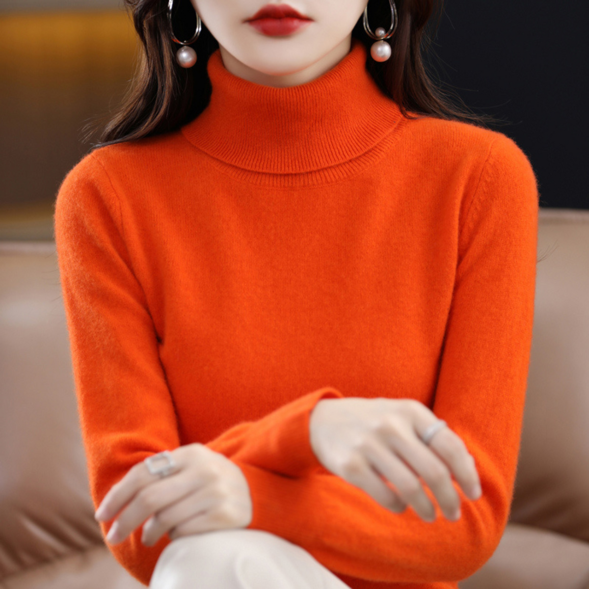 Orange polotröja med hög krage buren av en sittande modell med handen vilande på armen. 10